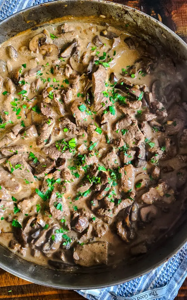 beef stroganoff in saucepan garnished with parsley resting on blue kitchen towel