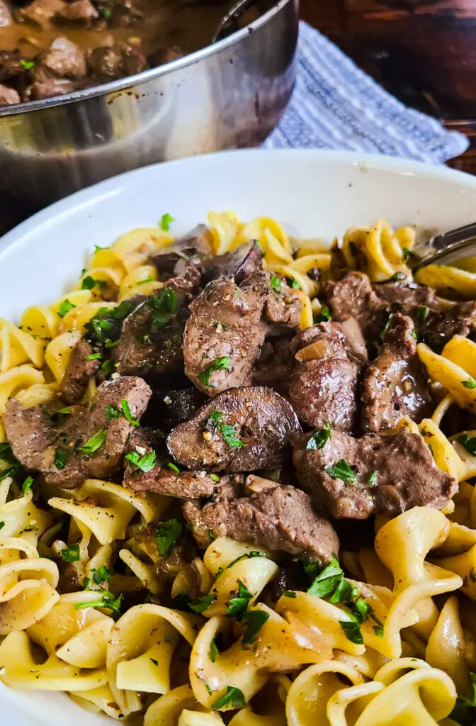 close up image of beef and mushrooms in gravy served over egg noodles. beef stroganoff