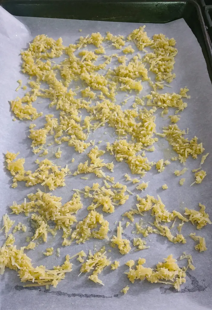 image of scattered parmesan and panko breadcrumb mixture on parchment paper line baking sheet.