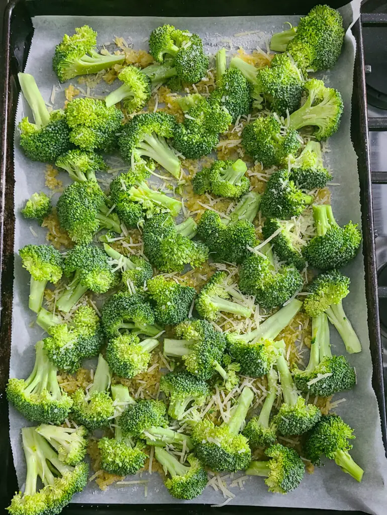 image of raw broccoli florets on parchment lined baking sheet with panko breadcrumbs and parmesan cheese