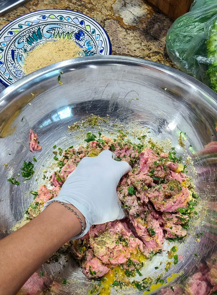 hand wearing latex gloves mixes ingredients to make chicken piccata meatballs in stainless steel mixing bowl