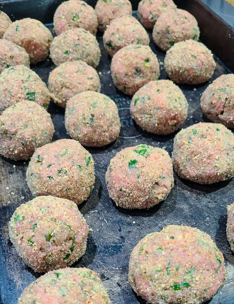 rolled and breaded chicken piccata meatballs lined up on baking sheet