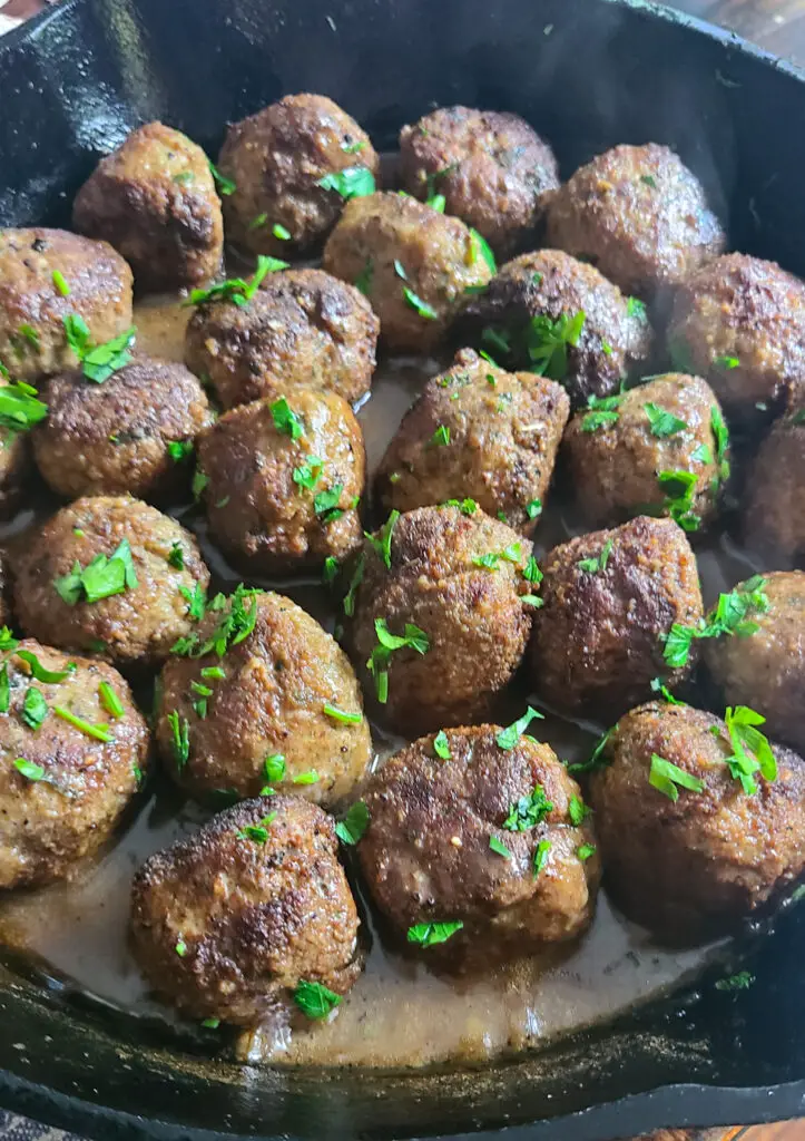 cast iron pan with seared chicken piccata meatball in lemon sauce garnished with chopped parsley