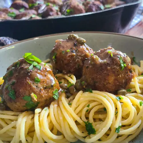 landscape image of chicken piccata meatballs on a bed of spaghetti