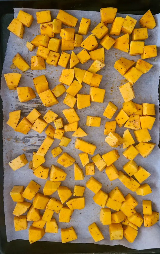 raw cubed butternut squash on parchment lined baking sheet