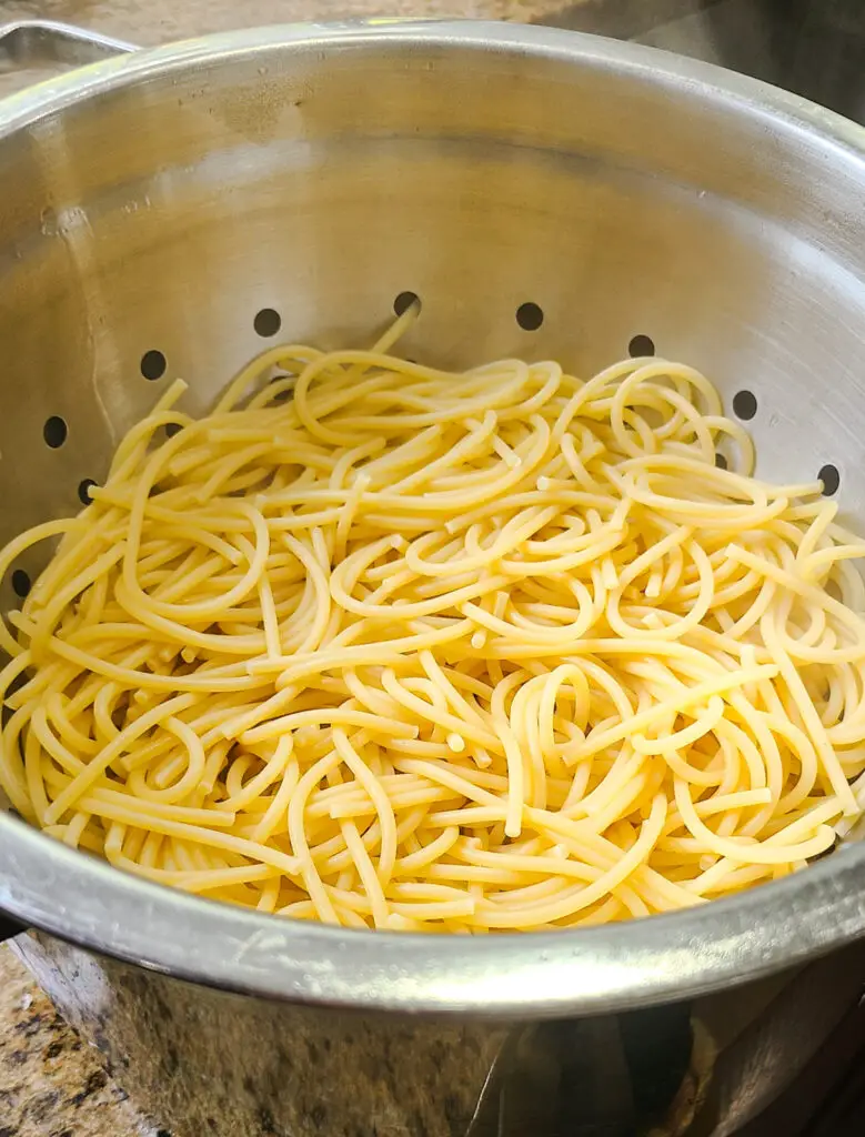 al dente cooked spaghetti in colander set in sink to drain