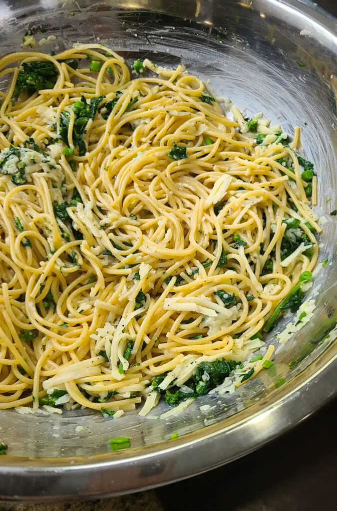 large mixing bowl containing cooked spaghetti, chopped broccoli rabe, shredded cheese, milk eggs, salt and pepper. 