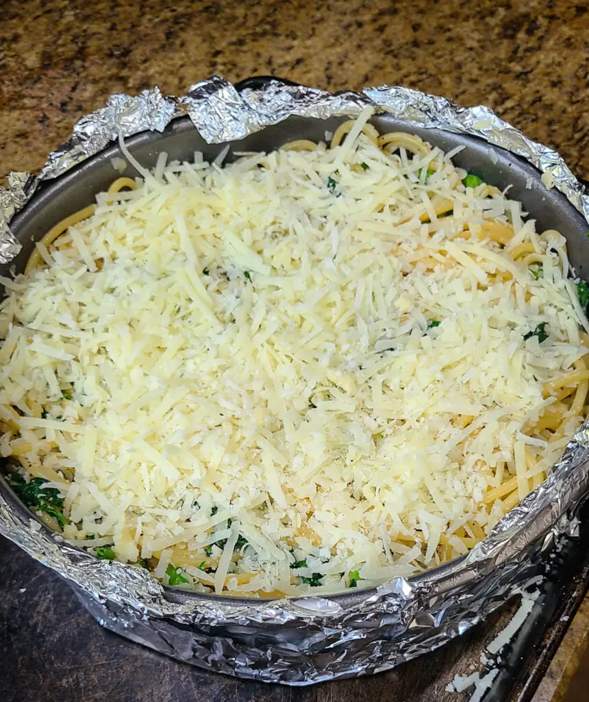 prepared springform pan with uncooked spaghetti pie and grated cheese layered on top