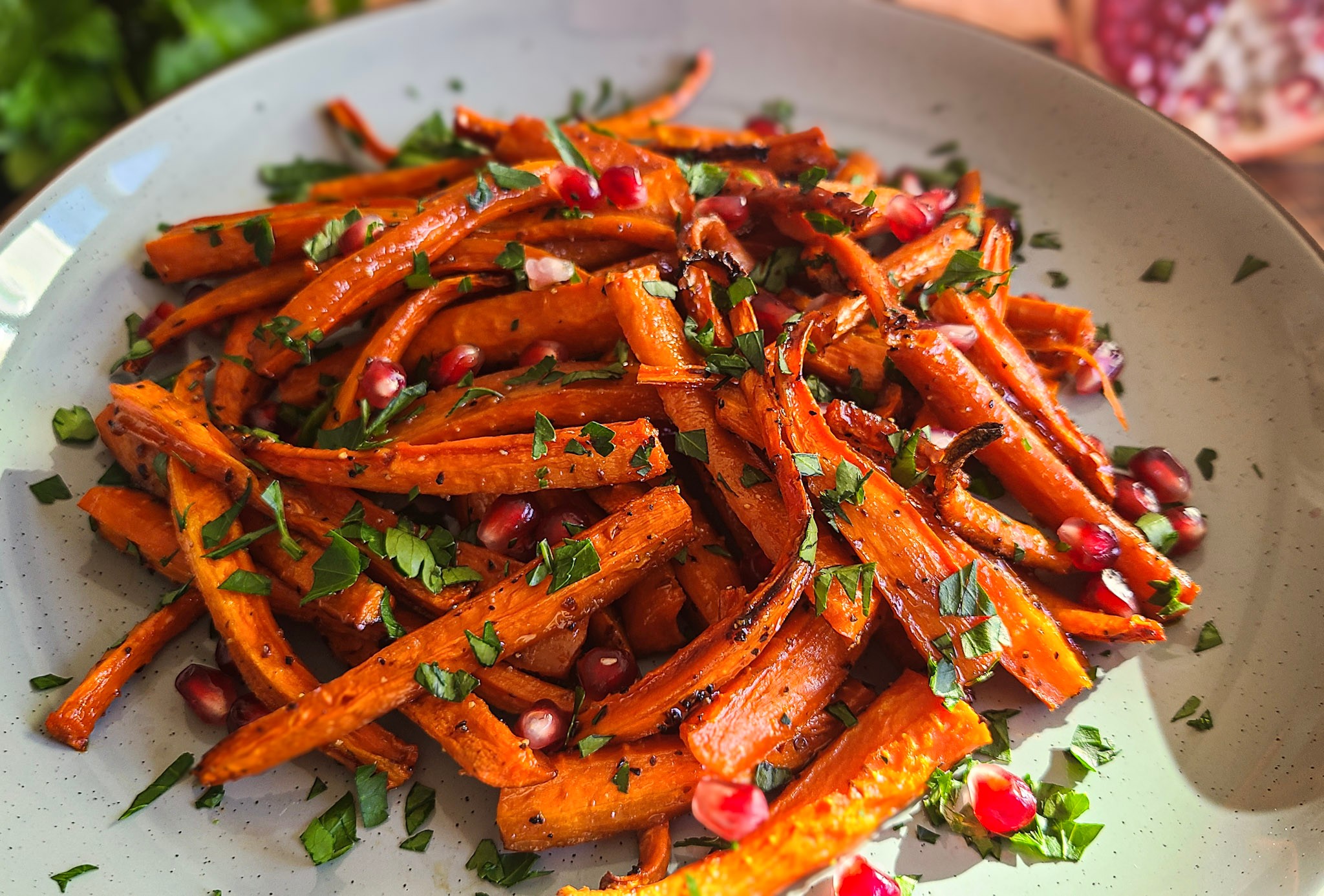 image of vibrant orange roasted quartered carrots sticks with carmelized edges. Garnished with parsley and pomegranate seeds